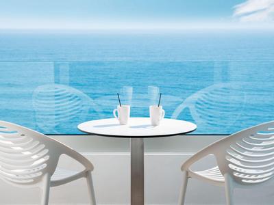 Two white chairs and a table on a balcony overlooking the sea under clear sky