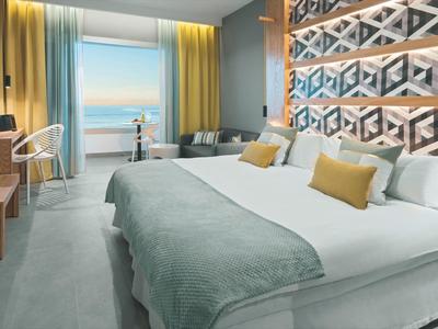 Modern hotel room with large bed, sea view, and bright, inviting decor.