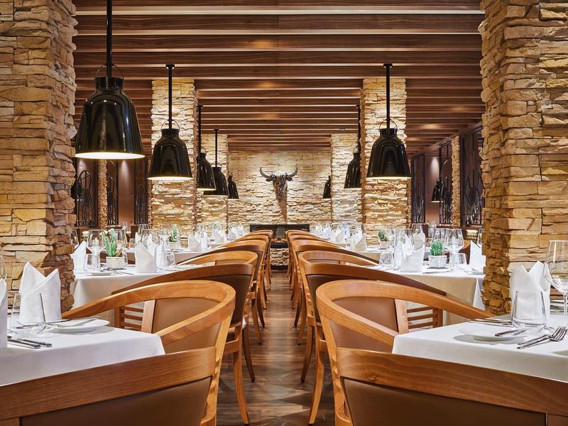 Cozy restaurant interior with stone walls, wooden beams, and set dining tables with chairs.