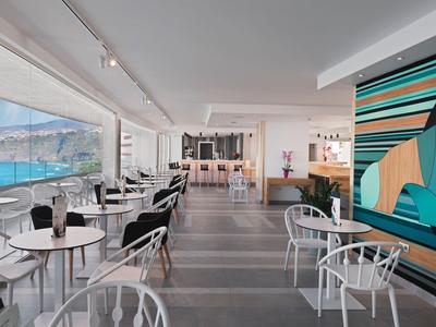 Ristorante moderno con finestre panoramiche sul mare, interno luminoso e arte murale colorata.