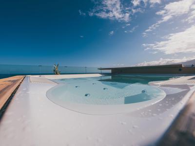 Vasca idromassaggio rotonda con cornice in legno, mare e cielo azzurro sullo sfondo.