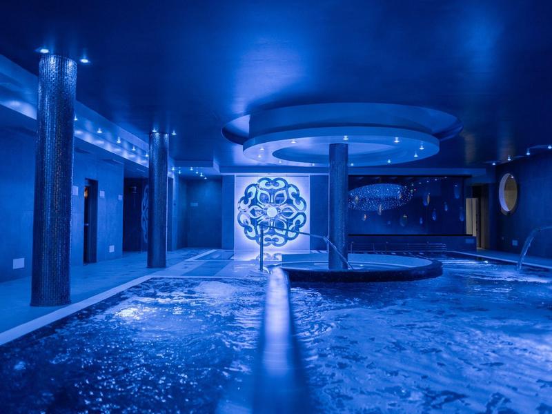 Vnitřní bazén s modrým osvětlením a kulatým sloupem v luxusním hotelu