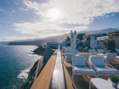 Terrazza sul tetto con sedie e tavoli bianchi con vista sul mare e montagne al tramonto.