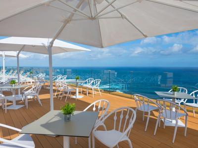 Terrasse mit weißen Tischen und Stühlen unter Sonnenschirmen mit Meerblick