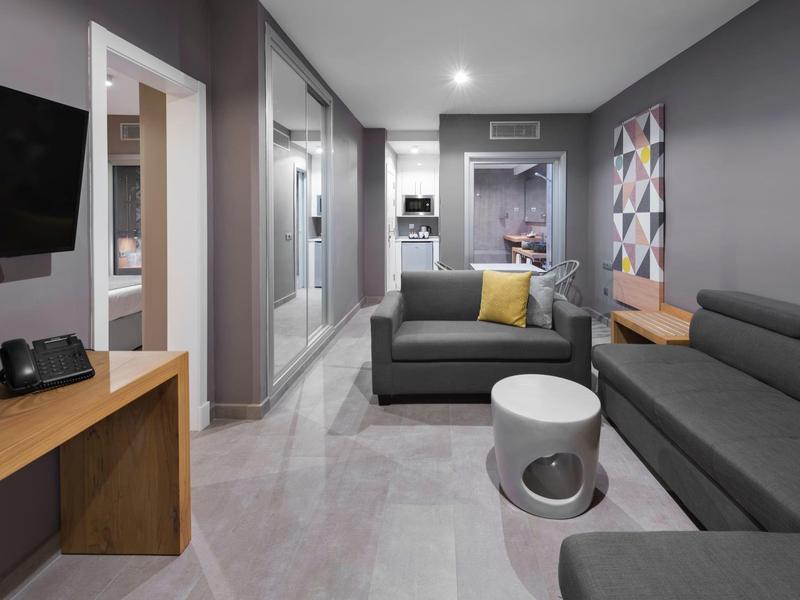 Moderner Hotelwohnraum mit grauen Sofas, Beistelltischen und grafischer Wandkunst.