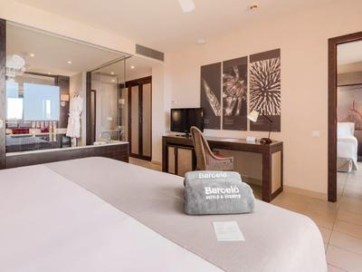 Modernes Hotelzimmer mit großem Bett, Schreibtisch, Stuhl und Bad im Hintergrund zu sehen.