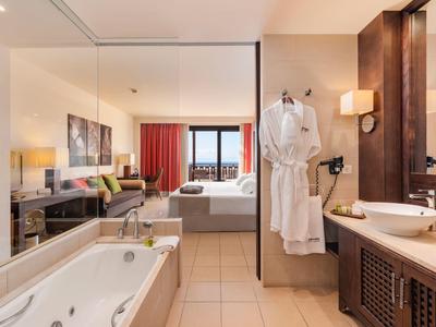Modernes Hotelzimmer mit Badewanne, Waschbecken, bequemen Bett und Balkon mit Aussicht.