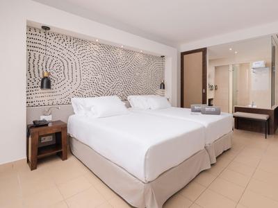 Habitación de hotel moderna con dos camas individuales, mesita, arte en la pared y baño abierto.