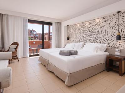Helles Hotelzimmer mit Doppelbett, Schreibtisch und Balkon mit Blick auf Gebäude.