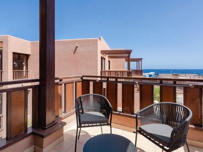 Balkon mit zwei Stühlen und kleinem Tisch, Blick auf das Meer bei klarem Himmel