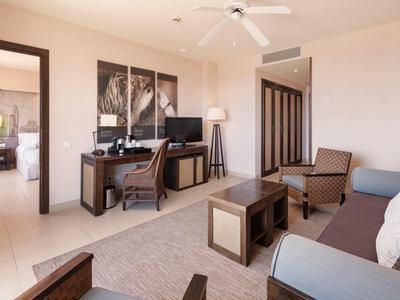 Bright hotel lounge with sofa, wooden table, desk, chair, and ceiling fan.