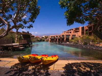 Two kayaks by a resort pool under clear blue sky framed by trees.