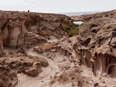 Rocky landscape with eroded formations and sparse vegetation near a body of water.