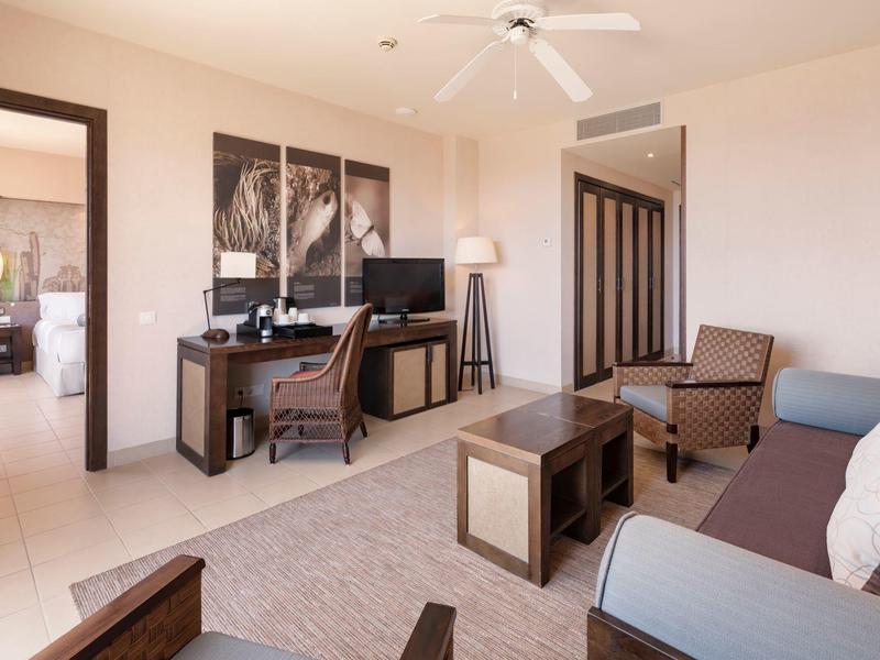 Bright hotel lounge with sofa, wooden table, desk, chair, and ceiling fan.