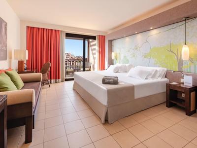 Nowoczesny pokój hotelowy z dużym łóżkiem, sofą, balkonem i miękkim oświetleniem.