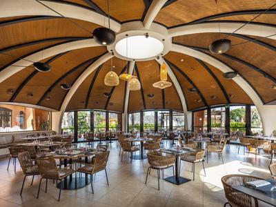Amplia zona de comedor del hotel con bóveda de techo de madera redonda y paredes de vidrio con vista al exterior.