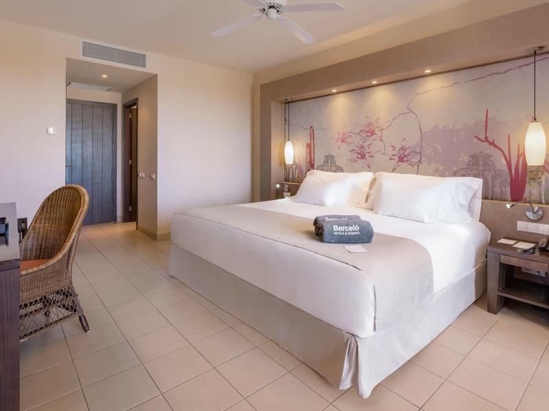 Nowoczesny pokój hotelowy z łóżkiem podwójnym, biurkiem, wiklinowym krzesłem i minimalistycznym wystrojem.