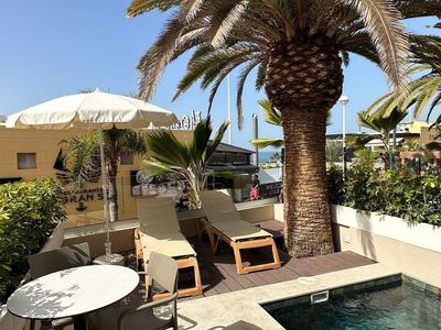 Hotelecke mit Pool, Sonnenliegen, Sonnenschirm und großer Palme unter blauem Himmel.