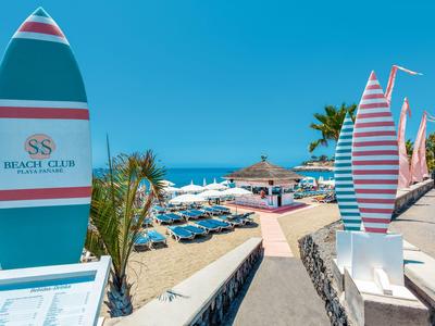 Strand mit Liegestühlen, Sonnenschirmen und bunten Surfboards am Eingang.