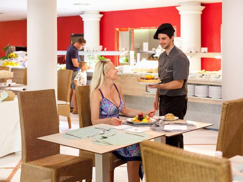 Serveur servant un plat à un client dans un restaurant avec un mur rouge et un buffet.