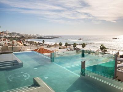 Infinity pool with sea view and beach in the background under cloudy sky