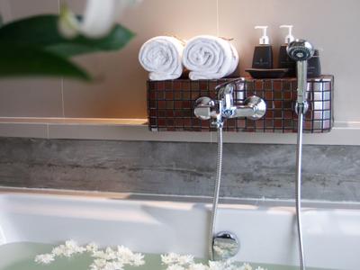 Badewanne mit warmem Wasser, weißen Blüten und gefalteten Handtüchern im Hintergrund