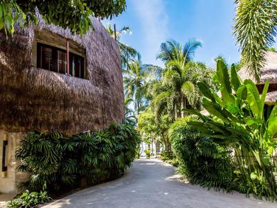 Ein tropischer Weg mit Palmen und grünem Laub, gesäumt von traditionellen strohgedeckten Häusern.