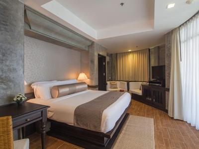 Modernes Hotelzimmer mit großem Bett, Schreibtisch, Fernseher und Vorhängen an großen Fenstern.