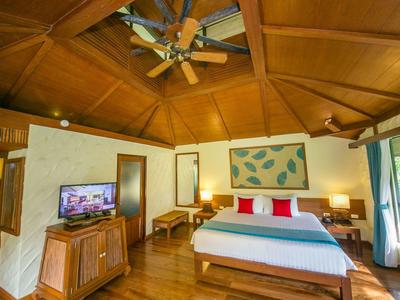 Helles Hotelzimmer mit Holzdecke, Doppelbett, TV, Ventilator und Zugang zu einem Balkon.
