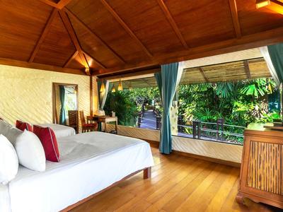 Helles Hotelzimmer mit Holzboden, bequemem Bett und Blick auf üppige tropische Vegetation.