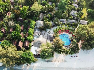 Vogelperspektive eines Resorts mit Pool, umgeben von tropischem Grün und Strand.