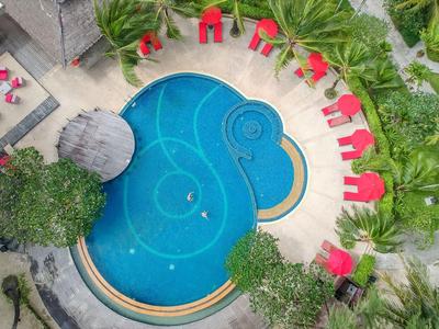 Ein blauer, tropfenförmiger Pool umgeben von roten Liegestühlen und grünen Pflanzen in einem Hotelbereich.