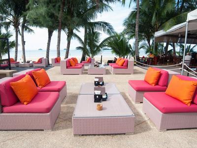 Strandlounge mit rosa Sofas, orangen Kissen und Blick auf Palmen und Meer.