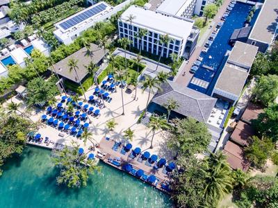 Luftaufnahme eines Strandresorts mit Pools, Liegestühlen und Palmen entlang des Meeres.