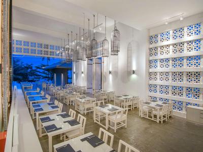 Modernes Restaurant mit weißen Tischen und Stühlen, Hängelampen und blauem Abendlicht draußen.