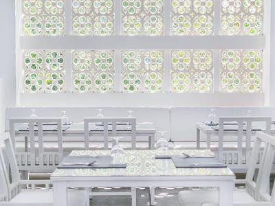 Helles, weiß eingerichtetes Restaurant mit eleganten Stühlen und dekorativen Fenstern.