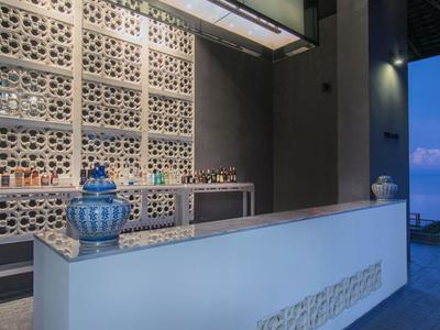 Moderner Hotelbarbereich mit weißer Theke, dekorativen Wandpanelen und Blick auf das Meer bei Abenddämmerung.