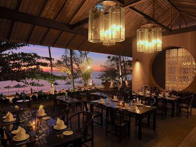 Gemütliches Restaurant mit Blick auf den Sonnenuntergang und den Ozean, warm beleuchtet und elegant gedeckt.