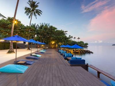 Holzsteg mit blauen Sonnenschirmen und Kissen am ruhigen Meer bei Sonnenuntergang