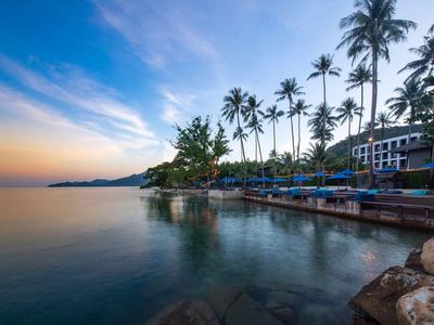 Küstenlinie bei Sonnenuntergang mit Palmen und ruhigem Wasser neben einem Hotel.