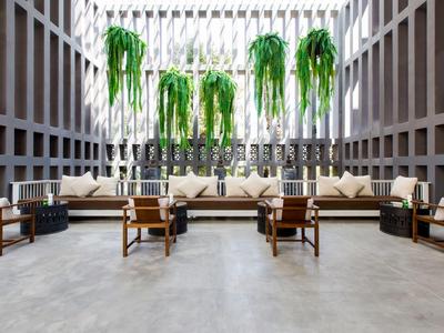 Helles Hotel-Lounge mit hohen Fenstern, hängenden Pflanzen und moderner Holz- und Lederbestuhlung.