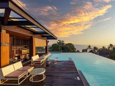 Moderne Terrasse mit Pool und Sonnenliegen bei Sonnenuntergang mit weitem Blick aufs Meer.