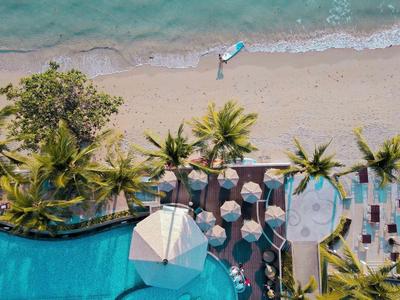 Vogelperspektive eines Pools neben einem Strand mit Palmen und Sonnenschirmen