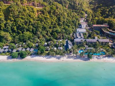 Luftaufnahme eines Resorts am Strand mit türkisblauem Wasser und dichtem grünen Wald im Hintergrund.