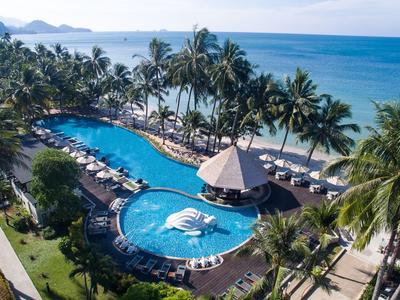 Großer Pool in tropischer Hotelanlage mit Palmen und Meer im Hintergrund.