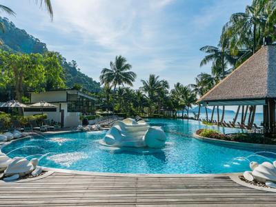 Ein Resortpool mit Tischen und Stühlen auf dem Wasser, umgeben von Palmen und Bergen.