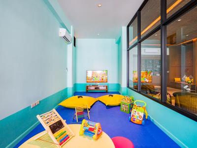 Helle Kinderspielecke mit buntem Boden, Tischen, Stühlen und Spielzeug im Innenbereich.