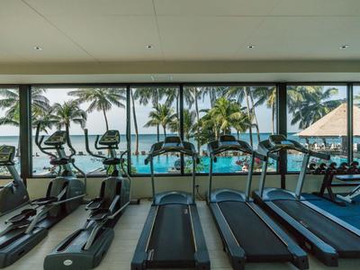 Fitnessraum mit Laufbändern und Blick auf tropischen Poolbereich mit Palmen.