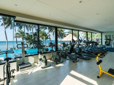 Helles Fitnessstudio mit Meerblick und modernen Trainingsgeräten neben einem Pool.