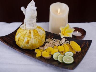 Wellness-Set mit Kräuterkompresse, geschnittenem Ingwer, Limetten, Kerzen und Blume auf Holztablett